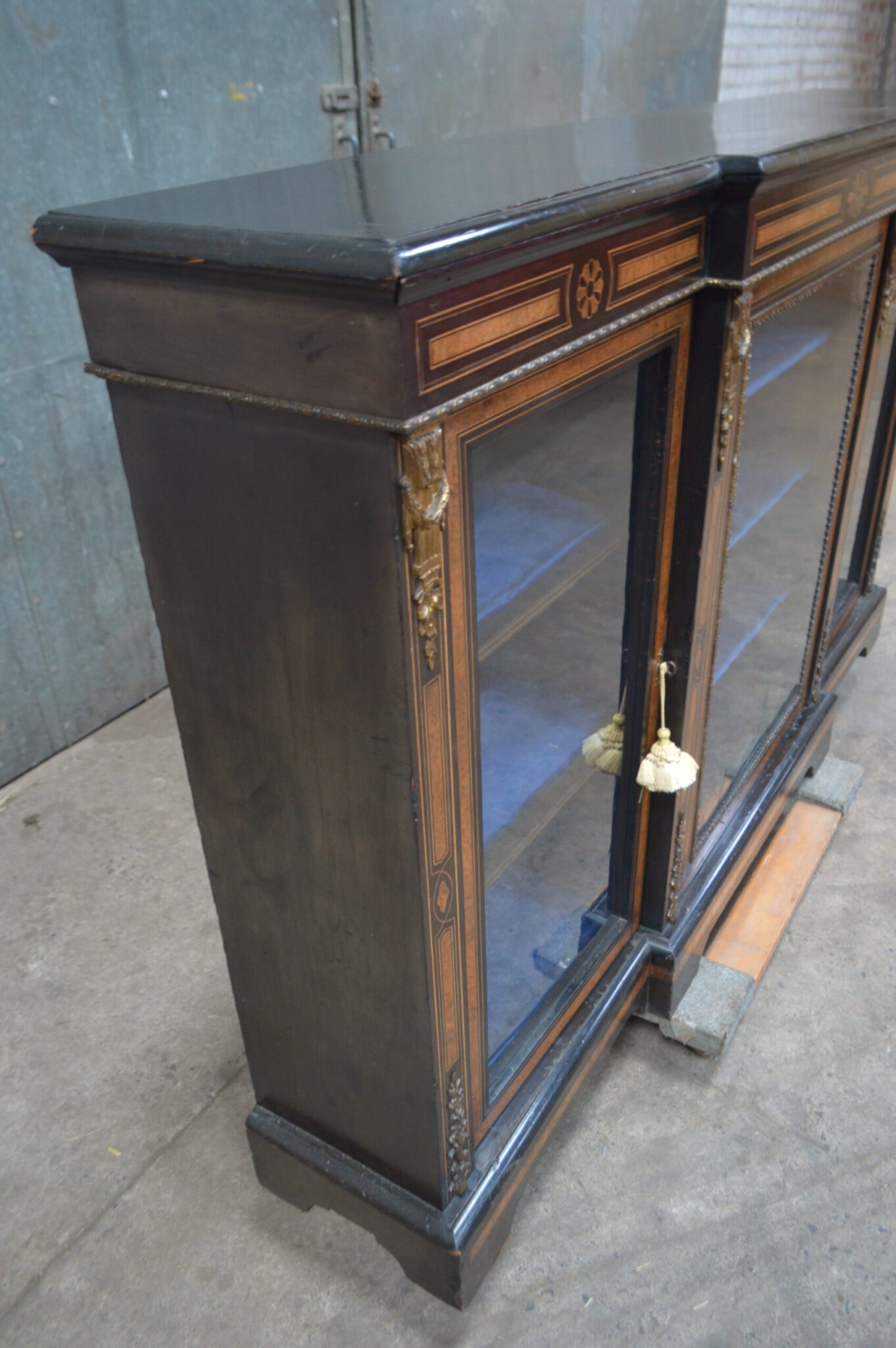 A Victorian amboyna and inlaid ebonised three-door breakfront bookcase.